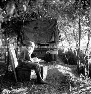 Hermann Hirchenhein schreibend, hinter einem LKW im Wald