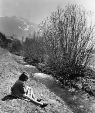 Kinderbilder. Allgäu im Frühling. An einem Bachufer sitzendes Mädchen