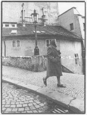 Ältere Frau mit Kopftuch läuft auf dem Bürgersteig (Altersgruppe 14-17)