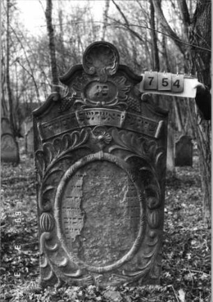 Grabstein 754 (Index: 99751601) Material: Sandstein Zustand: Schrift abgeblätt/fast völl. Textverlust Maße HxBxT: 164x83x12 cm Beschreibung: Stele, geschwungener Abschluß, ovales Schriftfeld eingetieft Symbolik: Trauben, Muschel, Blätter, Girlande, Band: Grabstein 754