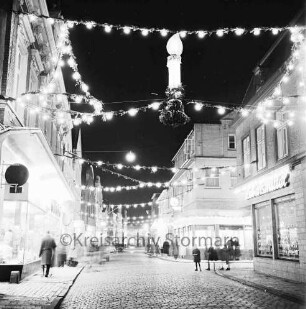 Mühlenstraße mit Adventsbeleuchtung: Passanten und parkende Pkw, links das Kaufhaus Nickel, rechts Einmündung der Hindenburgstraße, Blick Richtung Süden