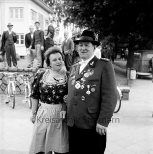 Ahrensburger Schützengilde: Schützenfest und Kreisverbandsfest: Stormarnplatz: Schützengilde-Kommandeur Walter Hauschildt mit Ehefrau Elfriede Hauschildt: hinten abgestellte Fahrräder, Mauer, Personen, Kleintransporter, Bäume: links im Hintergrund Bruno-Bröker-Heim