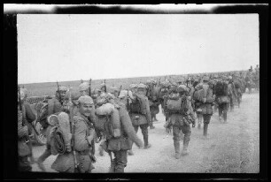 Nicht identifizierbare Gegend in Nordfrankreich oder Belgien: Soldaten mit Pickelhaube und voller Marschausrüstung auf einer unbefestigten Landstraße (Rückansicht) ("Infanterie auf dem Marsch")