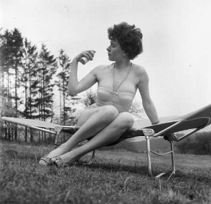 Frau in einem Garten auf einer Campingliege sitzend und sich mit Sonnenschutzmittel einsprühend