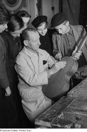Gitarrenbauer beim Polieren des Instrumentes umringt von Gästen auf der Weihnachtsausstellung im Alten Rathaus "Klingendes Vogtland"