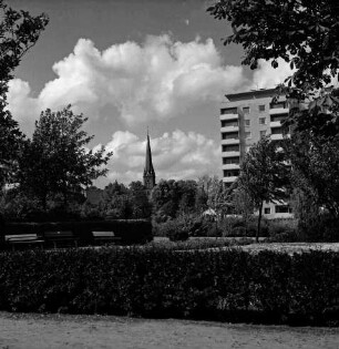Kurpark: vorn Grünfläche mit Blumen, Hecke, Bänke, Büsche und Bäume: hinten rechts Hochhaus "Liebe" an Kurparkallee: hinten Mitte Turm der Peter-Paul-Kirche