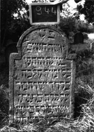 Grabstein 944 (Index: 100103843) Material: Sandstein Zustand: gut erhalten, etwas eingesunken Maße HxBxT: 96x57x10 cm Beschreibung: Stele, unregelmäßiger Hufeisenbogenabschluss, Schriftfeld eingetieft: Grabstein 944