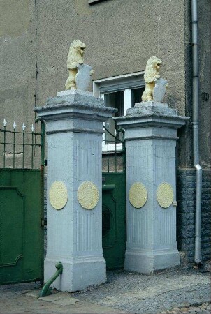 Eingang zu einem Bauernhof in Pohlitz: Säulen mit Löwenskulpturen auf Schildern, schmiedeisernes Hoftor und Personenfporte