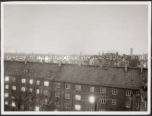 Blick vom Dach auf ein großes Wohnhaus mit zum Teil erleuchteten Fenstern (Altersgruppe 14-17)
