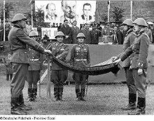 Waren (Müritz). Nationale Volksarmee - Landstreitkräfte. Öffentliche Vereidigung neu in das Panzerregiment 8 (PR-8) einberufener Wehrpflichtiger. Fahnenkommando (Mitte) und Schwursoldaten mit Hand an der entfalteten Truppenfahne