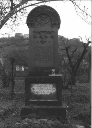 Grabstein 9 (Index: 99805013) Material: Sandstein Zustand: deutsche Inschrift im Sockel verwittert Maße HxBxT: 193x61x29 cm Beschreibung: Stele auf Doppelsockel mit Rundbogen, Inschriftennische rechteckig mit zwei Kleeblattbögen als Verzierung, Inschriftennische im Sockel querrechteckig Symbolik: Engel im Rundbogen, Blattornamentik am Rundbogen Besonderheit: kulturhistorisch wertvoll / künstl.-formale Gründe: Grabstein 9
