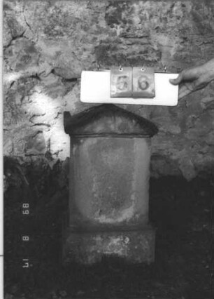 Grabstein 56 (Index: 100105678) Material: Sandstein Zustand: vollständig verwittert Maße HxBxT: 66x36x21 cm Beschreibung: Stele, getreppter Sockel, Giebel mit Akroteren Besonderheit: nebenan: Grabstelle ohne Stein: Grabstein 56