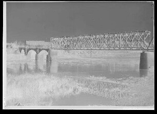 Staustufe Schweinfurt. Eisenbahnbrücke. Blick wie Bild 74 a-d, 1/2 Jahr später, auf die fertiggestellte neue Gerolzhofener Eisenbahnbrücke. Neu erstellt wurden der als Auflager für den alten und neuen Überbau dienende Pfeiler in Bildmitte, der Zwischenpfeiler zwischen künftigem Unterkanal und Saumain, das Widerlager (im Bild rechts) und der Überbau mit Diagonal-Fachwerkstreben. An der Brücke angehängt die Mitteldruck-Wasserrohrleitung der Stadt Schweinfurt. Aufnahmestandpunkt: Wie Bild 74 a-d. Schweinfurter Pegel = 275 cm.