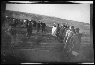 [Nador (?) (Marokko:] Reihe einheimischer Männer gegenüber locker stehenden anderen Einheimischen und Soldaten auf einem hoch gelegenen Feld