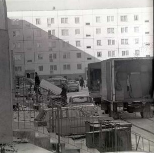 Einzug : Grimma. Neubausiedlung im Winter. Neue Bewohner beziehen eine Wohnung im Plattenbau. Zwei Möbelpacker tragen ein Möbel ins Haus