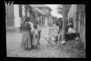 Odobești (=Rumänien): rumänische Frauen, Kinder und Männer am Rand einer grob gepflasterten Straße beim Betrachten einer Staffelei mit einem Bild eben dieser Straße