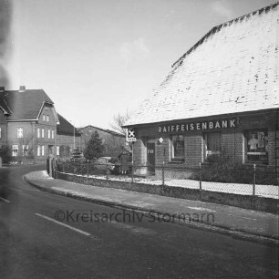 Lasbek-Dorf: Überfall: Raiffeisenbank Bad Oldesloe, Zweigstelle Lasbek: Steindamm: rechts Bankgebäude: links daneben Frau und Pkw: hinten links Bauernhäuser: Winter