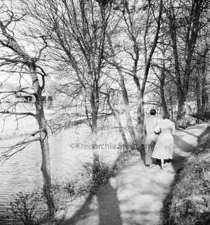 Trave: vorn Wanderweg mit Baumreihe am Ufer: rechts Paar: hinten links Badeanstalt: hinten rechts Brücke