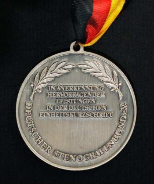 Silbermedaille Deutsche Meisterschaften in Kurzschrift und Maschinenschreiben in Ettlingen 1988 am schwarz-rot-goldenen Band : Sammlung Deutscher Stenografenbund. Silbermedaille Deutsche Meisterschaften in Kurzschrift und Maschinenschreiben in Ettlingen 1988 am schwarz-rot-goldenen Band. Messing, versilbert; Durchmesser 50 mm, Gewicht 39 g (1988; Deschler & Sohn, München). Dresden: SLUB R c 0549