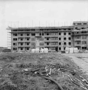 Fuchsberg / Im Hölk: Wohnblocks der Gemeinnützigen Wohnstätten Genossenschaft Bad Oldesloe: im Bau mit Gerüst: davor Baumaterial: vorn rechts gepflasterter Gehweg, links verkrautete Wiese