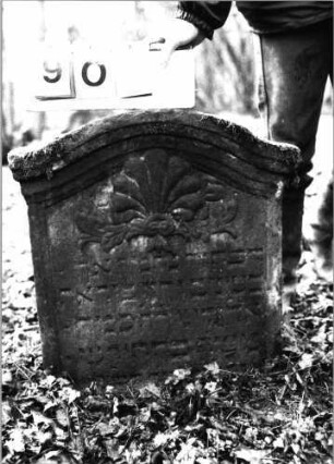 Grabstein 901 (Index: 99753240) Material: Sandstein Zustand: leicht verwittert/Stele eingesunken Maße HxBxT: 62x54x10 cm Beschreibung: Stele, Segmentbogenabschluß mit Verdachung, Schriftfeld eingetieft Symbolik: Lilie, Ranken: Grabstein 901