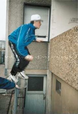 Junge versucht von einem Geländer auf eine Balkonbrüstung zu springen