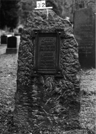Grabstein 32 (Index: 100092754) Material: Obelisk: Granit; Platte: Metall? Maße HxBxT: 154x70x40 cm Beschreibung: grobbehauener Obelisk mit aufgesetzter Schriftplatte: Grabstein 32 (1)