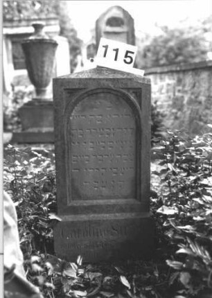 Grabstein 115 (Index: 100114277) Material: Sandstein Zustand: verwittert mit Textverlust Maße HxBxT: 80x38x18 cm Beschreibung: Stele, Sockel, obeliskenartiger Abschluß, eingetieftes Schriftfeld mit Rundbogen Besonderheit: Kindergrab: Grabstein 115