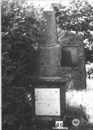 Grabstein 42 (Index: 99805382) Material: Granit, weiße Marmorplatte Zustand: Obelisk quer gebrochen und wieder zusammengefügt, gut Maße HxBxT: 198x50x28 cm Beschreibung: Obelisk auf Quaderblock mit vorspringender Abdeckplatte, Sockel, rechteckige Schriftplatte: Grabstein 42