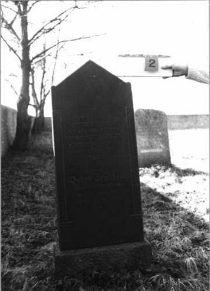 Grabstein 2 (Index: 100116070) Material: Granit, poliert Zustand: gut Maße HxBxT: 136x49x16 cm Beschreibung: aufgesockelte Stele mit eingezogenem, giebelartigem Abschluß Symbolik: Cohanim-Hände, Schofar Besonderheit: kulturhistorisch wertvoll / hist.-wiss. Gründe (Gemeindestellung): Grabstein 2