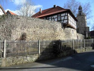 Kirchhofmauer im Südwesten mit Schulhaus vom Ort (im 19 Jhd aus einstigem Gaden umgebaut - Steinbrüstung des Wehrgangs mit Schießscharte erhalten)