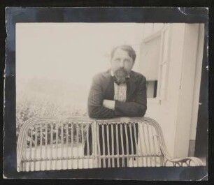Arthur Schnitzler im Nadelstreifenanzug auf eine Korbbank gelehnt im Garten