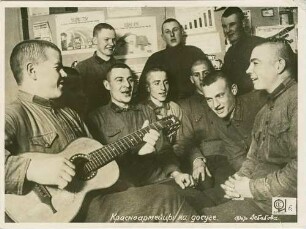 Rotarmisten in Mußestunde, zehn Sowjetsoldaten in Halbkreis teils stehend, teils sitzend beim Singen mit Gitarrenbegleitung in Kasernenzimmer