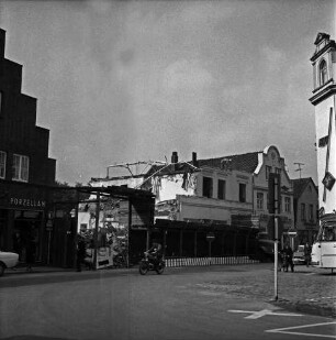 Firma Carl Hoffmann: Hindenburgstraße: Elektrohandel: Abriss des Firmengebäudes: davor Bauzaun: links Wohn- und Geschäftshaus des Haushaltswarenhandlung Otto Möller, links Wohn- und Geschäftshaus mit Schlachterei: rechts Verkehrsschilder, Fußgänger und Front eines Busses: in der Mitte Motorradfahrer