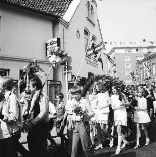 Kindervogelschießen: Umzug: beim Einbiegen von Hagenstraße in Hindenburgstraße: Gruppen der Königin-Luise-Schule mit Fähnchen "KLS", dabei Jungen mit Blumenstäben, Mädchen mit Blumenbögen: über Straße Wimpelgirlanden, 8. Juli 1970