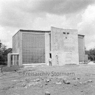 Katholische Heilig-Geist-Kirche: Wöhrendamm: Kirchengebäude vor Fertigstellung: Außenansicht von Südosten: Eingangsbereich mit Reliefs: hinten Mitte in Eingang Maler: vorn unbefestigte Außenanlage: hinten rechts und links Bäume