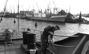 Hamburg-Steinwerder. Blick in den Kaiser-Wilhelm-Hafen mit kleinem Leuchtturm am Ellerholzhöft, hinten Schornsteine des Kraftwerks Neuhof. Das Deck eines Schiffes wird gesäubert
