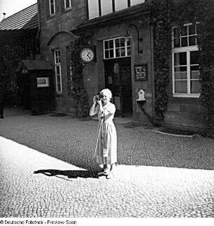 Touristin mit Fotoapparat vor dem Empfangsgebäude eines Bahnhofes