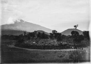 Siedlung : Blick von einer Anhöhe auf eine von Palisaden geschützte Siedlung.Im Hintergrund der Mount Meru von Wolken verhangen