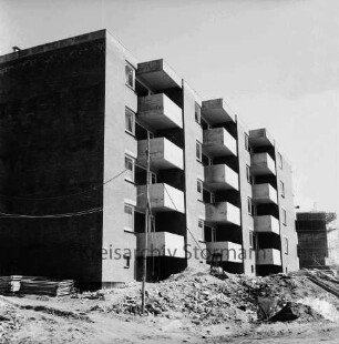 Ehmkenberg: Neubau: Wohnblock vor Fertigstellung: vorn Stapel mit Gerüsten, Erdhaufen, Bauschutt, Stromleitung: hinten rechts eingerüsteter Rohbau