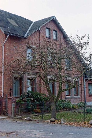 Fritz-Berodt-Straße 5: traufständiges Bauernhaus aus Backstein: Giebelseite Wohntrakt, links Quergiebel zu Straßenfront, rechts flacher Anbau: Garten, Obstbaum, Maschendrahtzaun