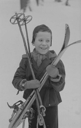 Kinder beim Ski- und Schlittenfahren, Junge mit Ski nach der Abfahrt