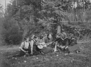 Jugendwandern : Jugendwandern. Mädchen und Jungen mit Klampfe inmitten einer Gruppe vor einem Landheim