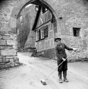 Rothenburg ob der Tauber. Blick gegen ein Wohnhaus nahe Rödertor, davor Turmbewohner des Röderturmes beim Straßefegen