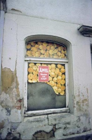 DDR. Mit Werbeplakat "Äpfel - Vitamine sind Trumpf" teilweise zugeklebtes Erdgeschoßfenster