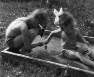 Kinderbilder. Zwei kleine Mädchen, in einem flachen Planschbecken sitzend