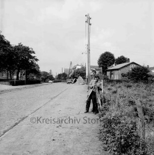 Rethwischdorf: B 208: Hauptstraße: Ortsdurchfahrt mit Kopfsteinpflaster: vorn rechts Mann bei Vermessungsarbeiten für Ausbau: dahinter Strommast: im Hintergrund Bauernhäuser