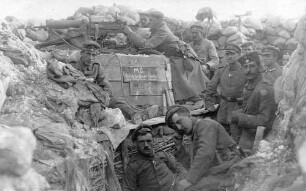 Elf Soldaten in einem ausgebauten Schützengraben mit MG-Stellung (auf Kiste "M.G. Ständig feuer bereit M.G. V") "Zum Andenken an den Weltkrieg von deinem Bruder Philipp (14/15/16)"