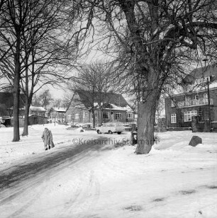 Dorfplatz und Dorfstraße: links Fußgängerin: Bäume mit Milchböcken und parkender Pkw: dahinter rechts Bauernhof Bockwoldt und weitere Bauernhäuser: Winter