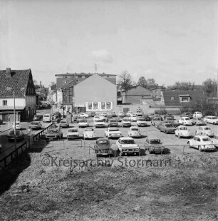 Hagenstraße / Weg am Bürgerpark: eingezäunter Baugrund für Neubau der Kreissparkasse Stormarn: Parkplatz mit Pkws: dahinter Werbeplakatwand und Wohn- und Geschäftshäuser